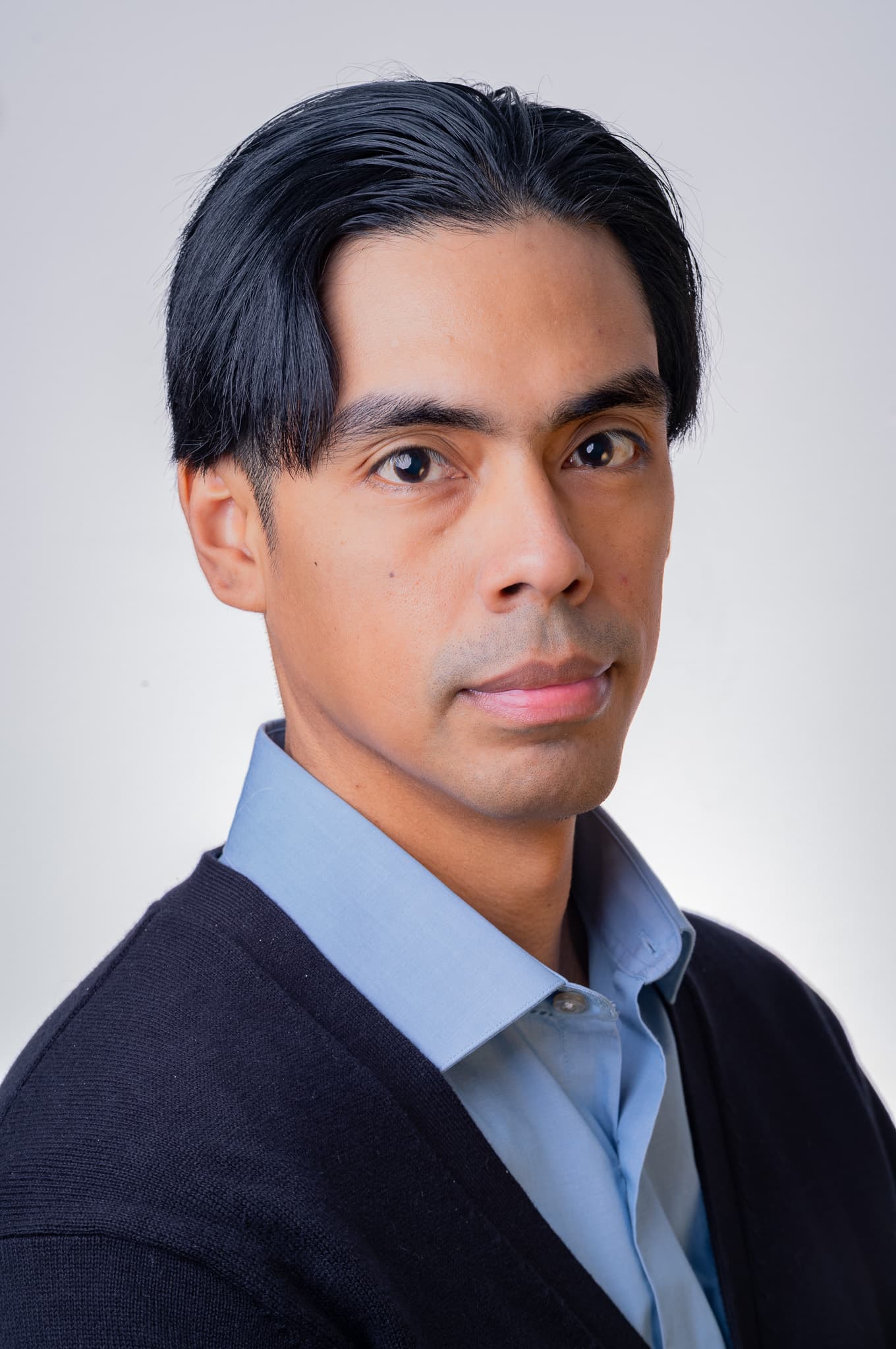 Man in a light blue shirt and navy cardigan, professional headshot on a light gray backdrop