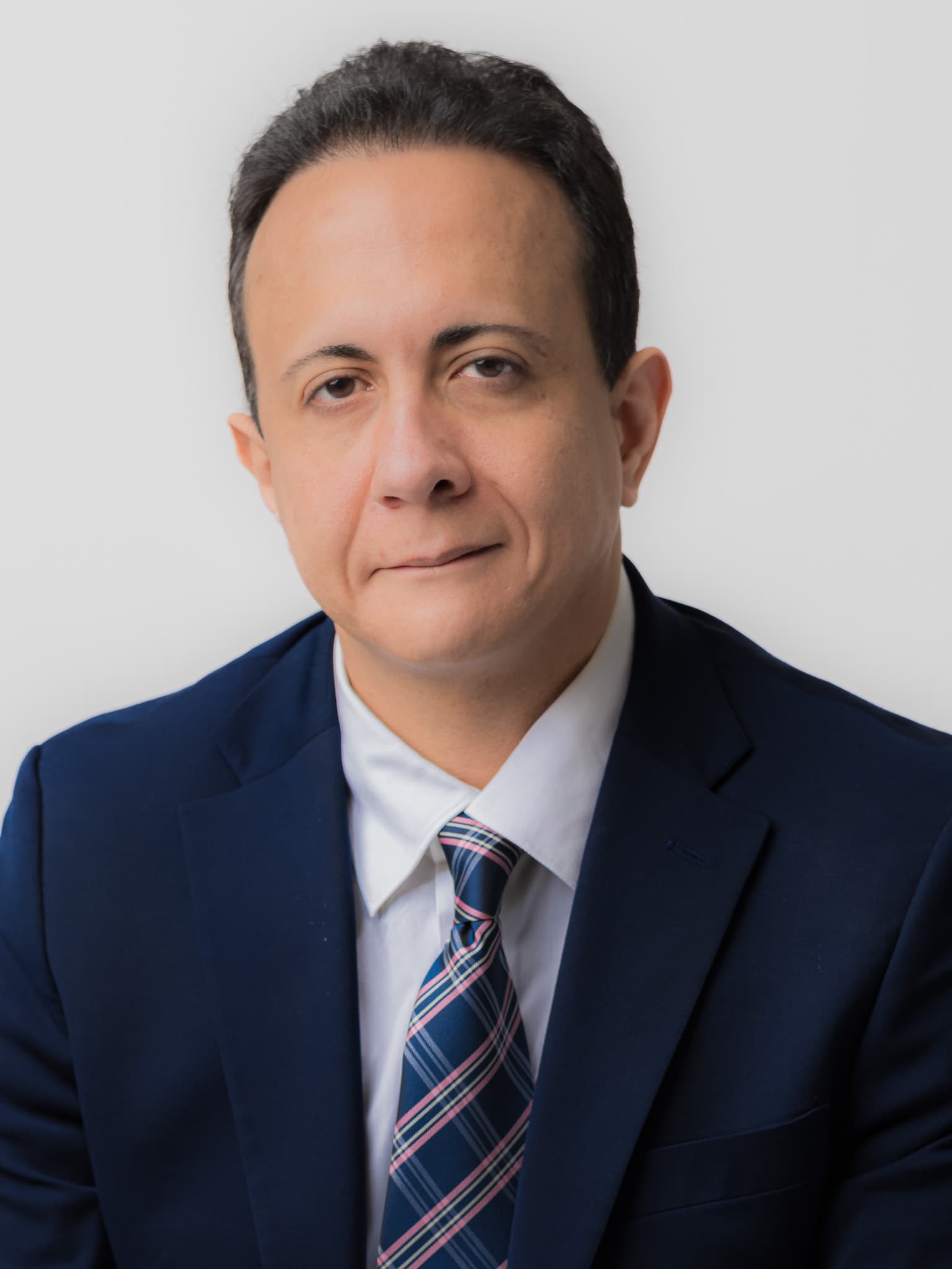 Man in a navy suit and striped tie, business headshot on a white background